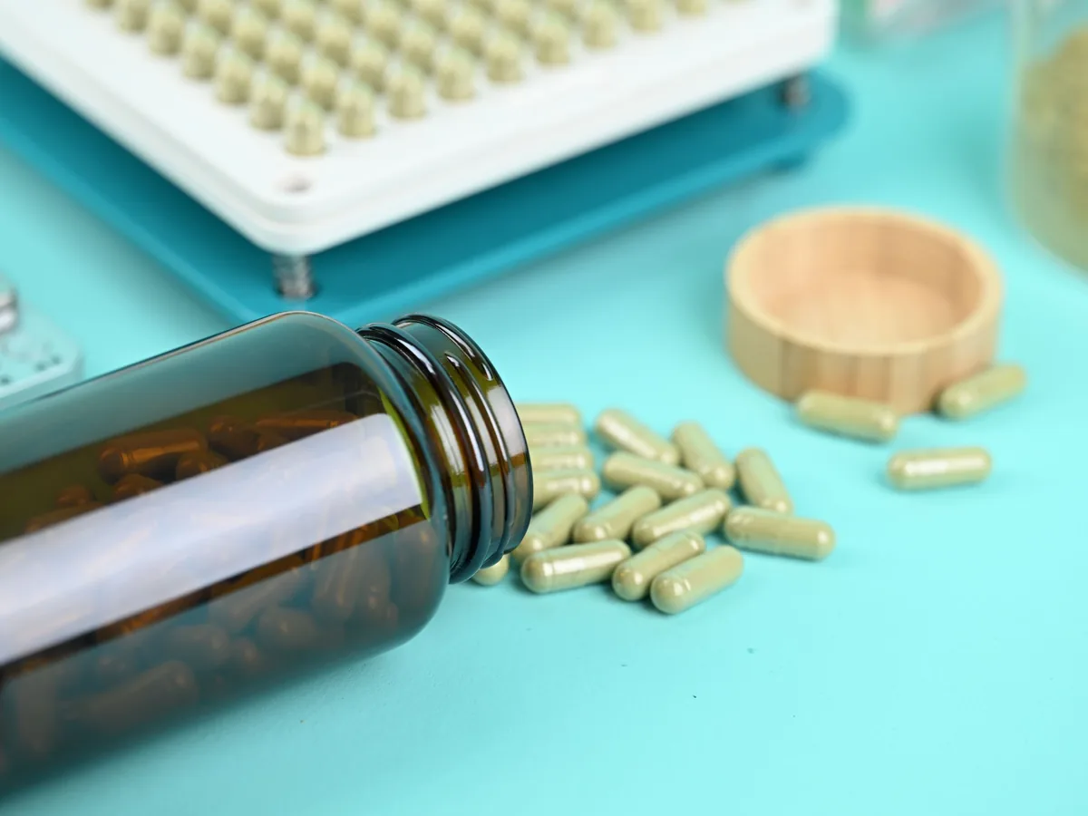 Capsules next to an amber supplement bottle and a capsule tray