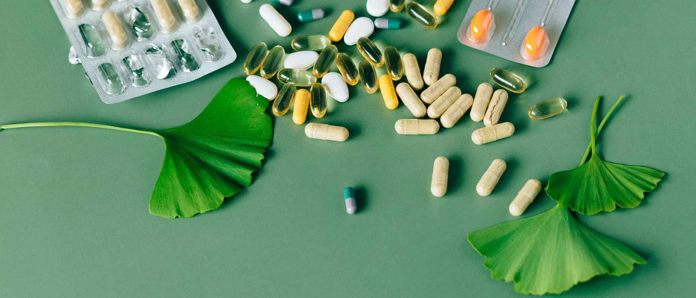 Herbal supplement capsules and ginkgo leaves on a green background