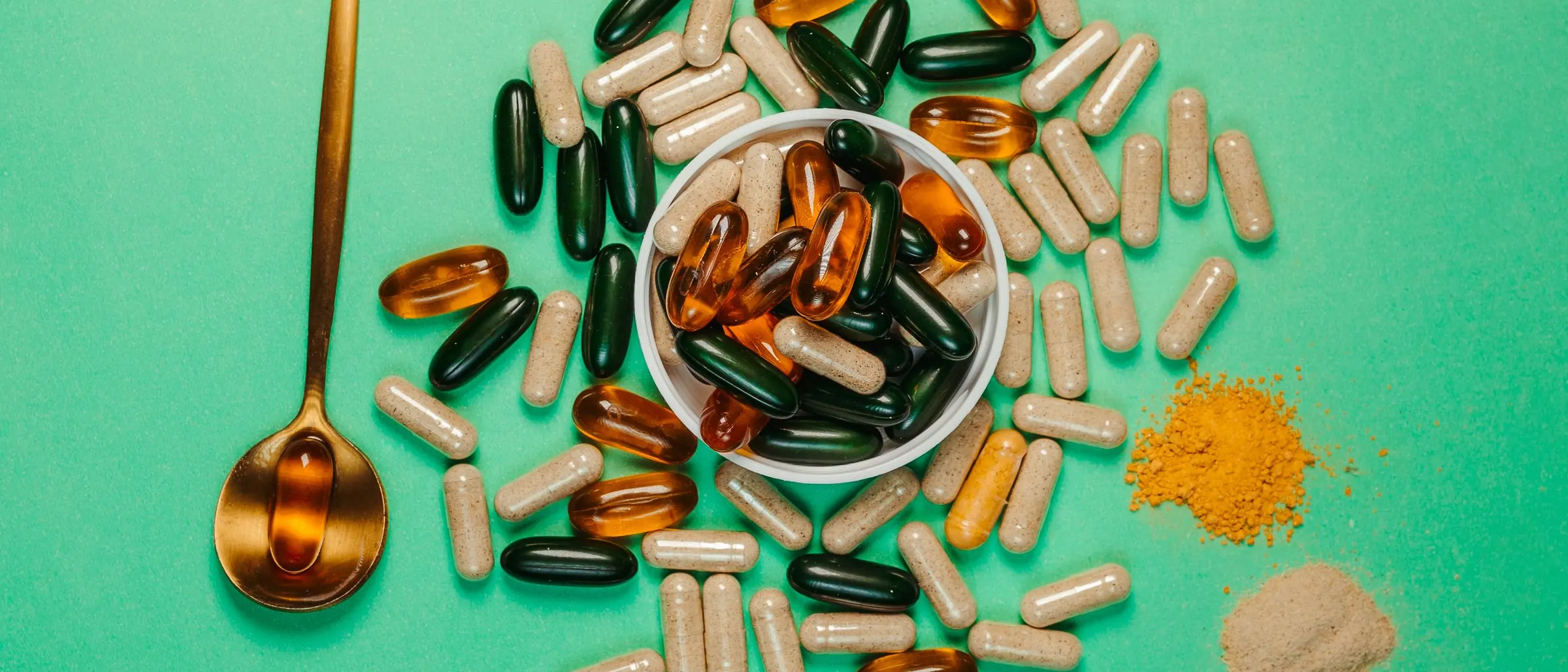 Assorted vitamin capsules and powders with a golden spoon on a green background