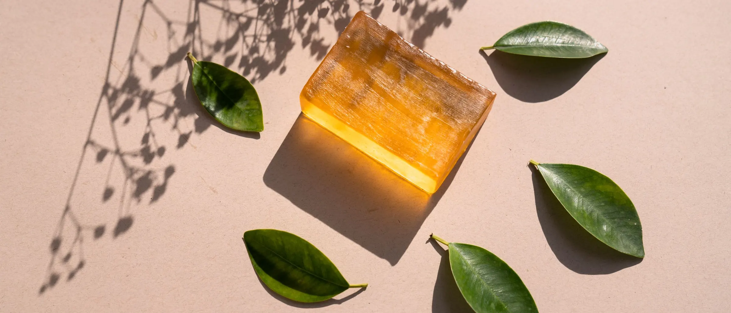Translucent amber soap bar with green leaves on a beige background