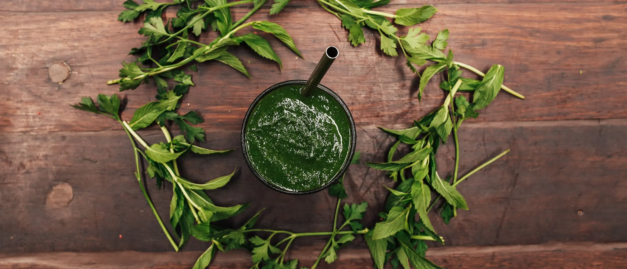 Green smoothie surrounded by fresh herbs on a wooden table